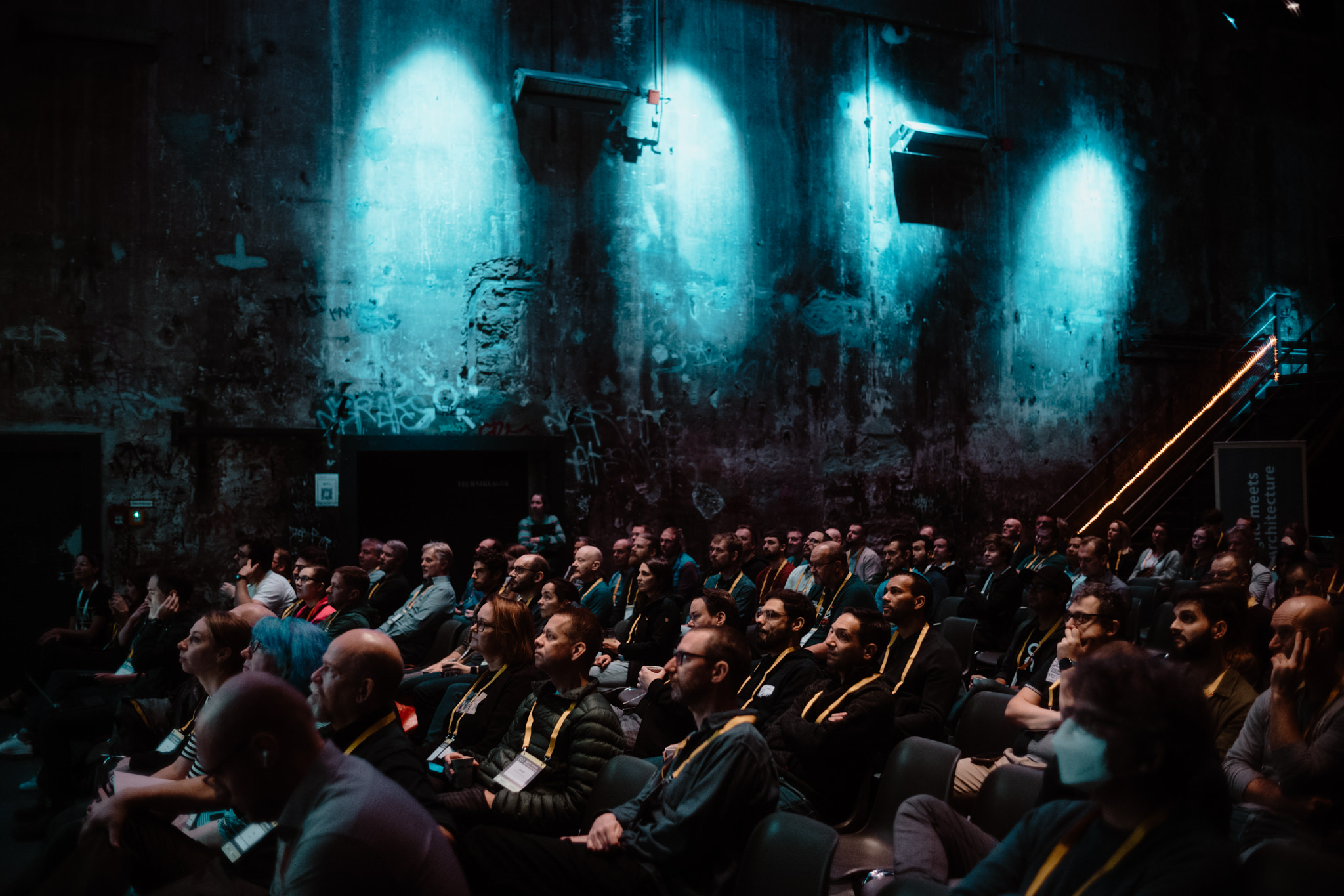 Audience in the Kesselhaus, its graffiti wall lit in teal